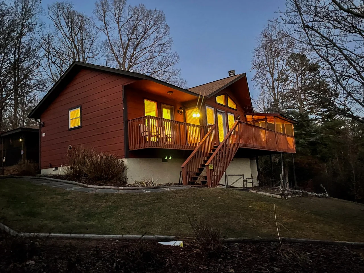 Dog-friendly cabin stay near Pigeon Forge TN: elevated burgundy cabin with glowing windows at dusk and a wraparound deck,
