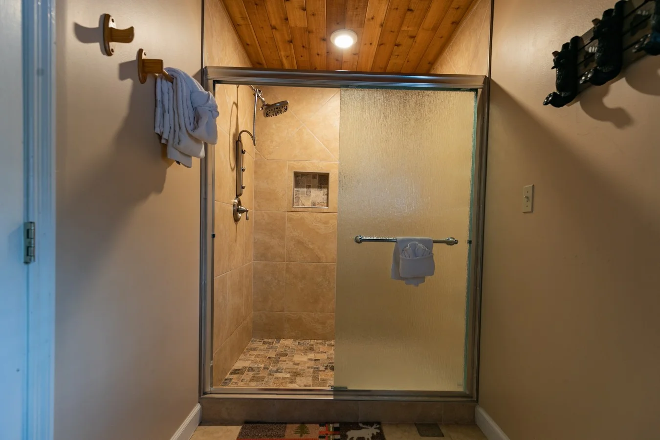 Walk-in shower with warm tan tile, rainfall showerhead, and rustic wood beams in a Gatlinburg, TN cabin by Bear Crest Cabins