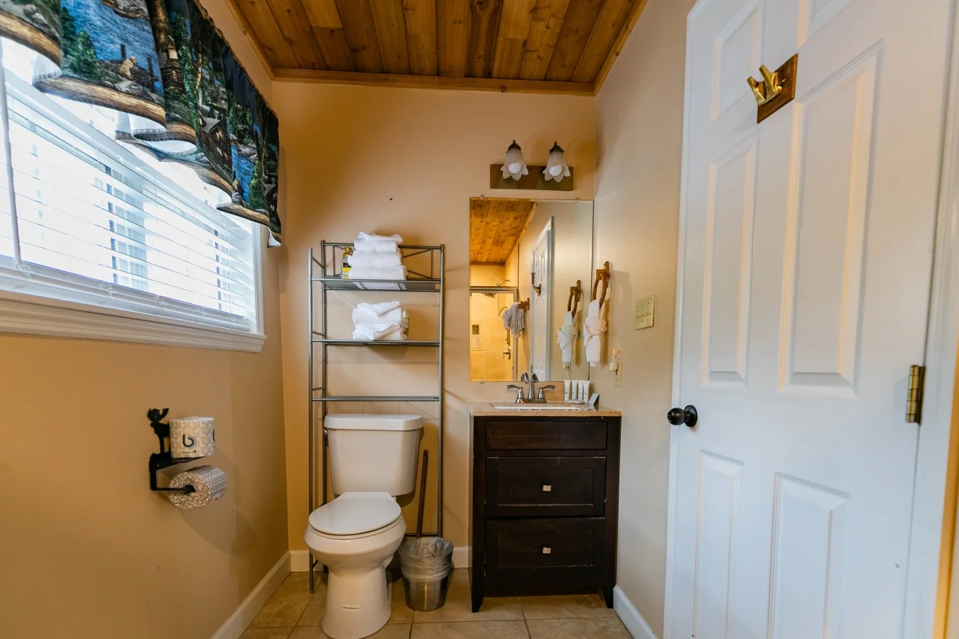 Bathroom with dark vanity, subway tile accents, wooden ceiling beams, and rolled towels in a Gatlinburg, TN cabin rental