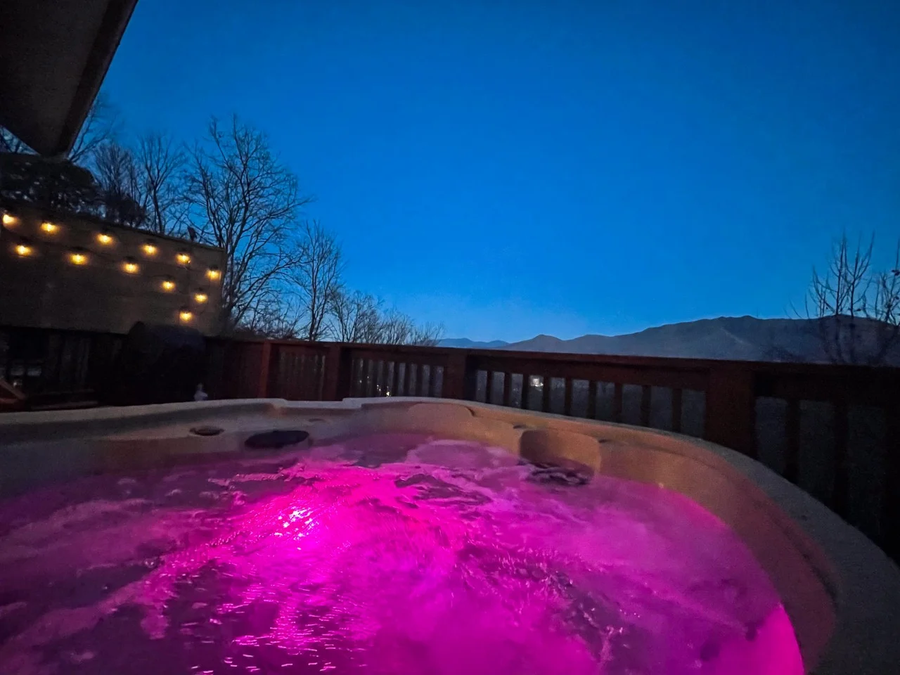 Illuminated hot tub glowing pink at dusk on a deck with mountain views, a Heavenly View cabin amenity in Gatlinburg, TN from