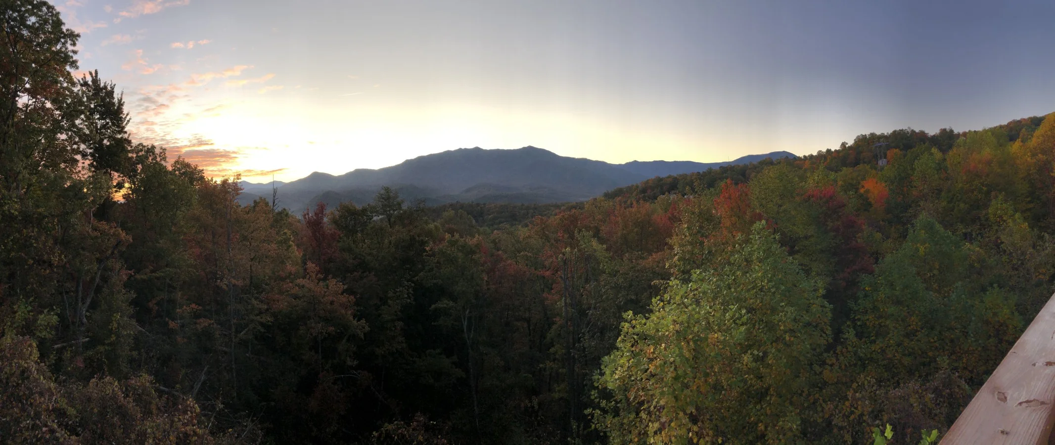 Sunset over rolling mountains and forested valleys with red, orange, and green autumn foliage, a Smoky Mountains scenic
