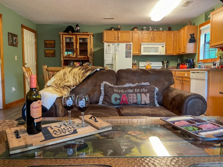Stone fireplace living room in a Sevierville, TN cabin with brown leather sofa, wood coffee table, and sage green kitchen.
