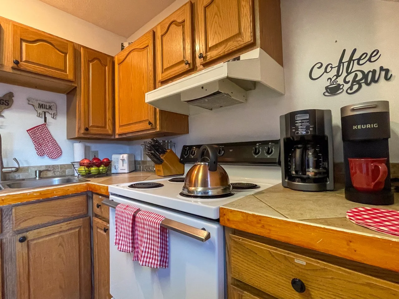 Fully stocked cabin kitchen with oak cabinets, white range, Keurig coffee maker, and red gingham accents in a Gatlinburg, TN